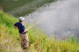 A man in a camo hat fishing in a river.
