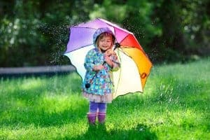 A little girl holding an umbrella during a sun shower.